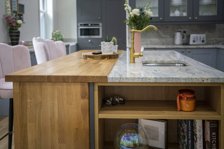 Island end view showing an Ivory Fantasy Granite worktop with inset sink, styled with flowers and accessories above open shelving.