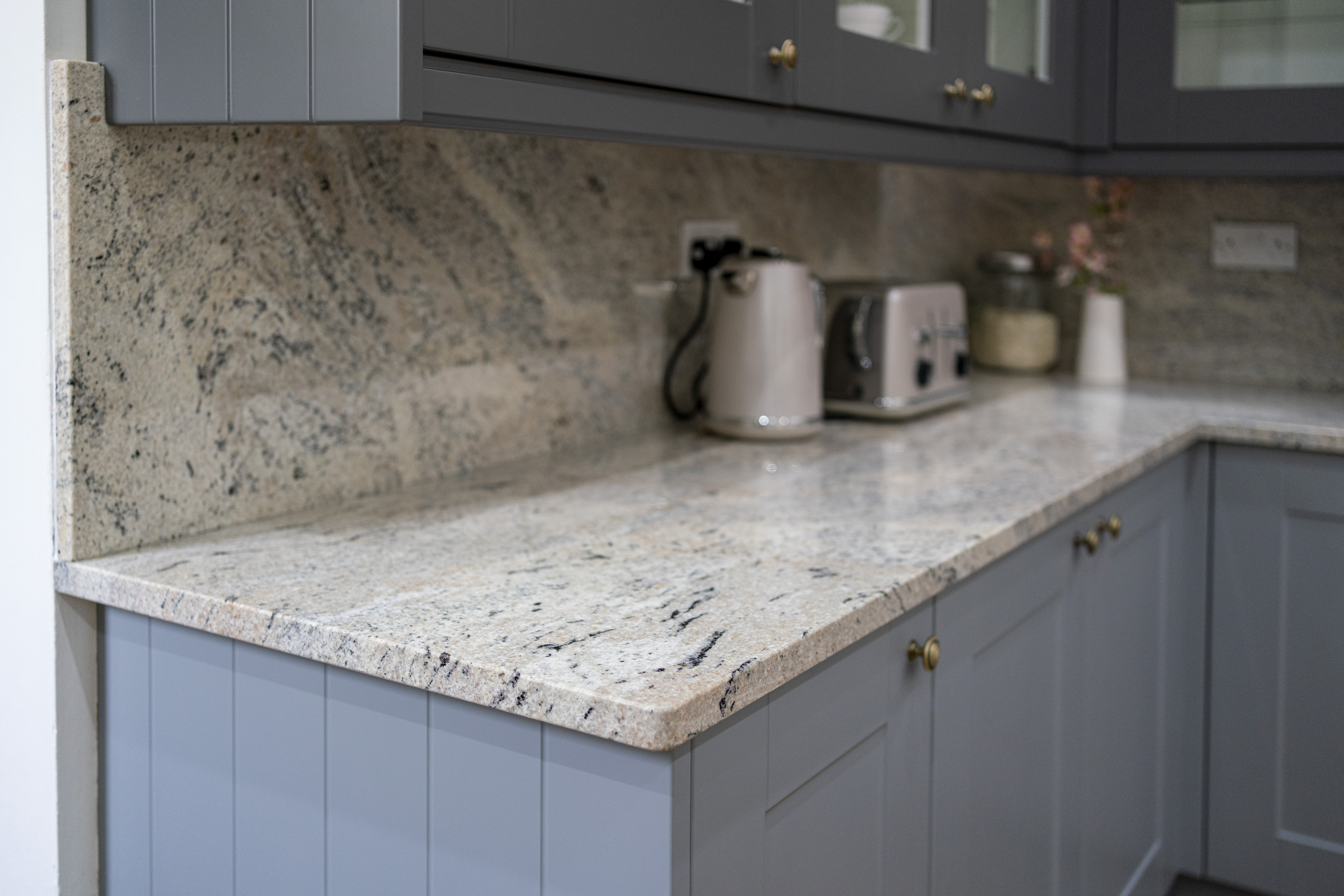 Corner view of Ivory Fantasy Granite worktop run with matching Granite upstand, shown with kettle and toaster on blue cabinetry.
