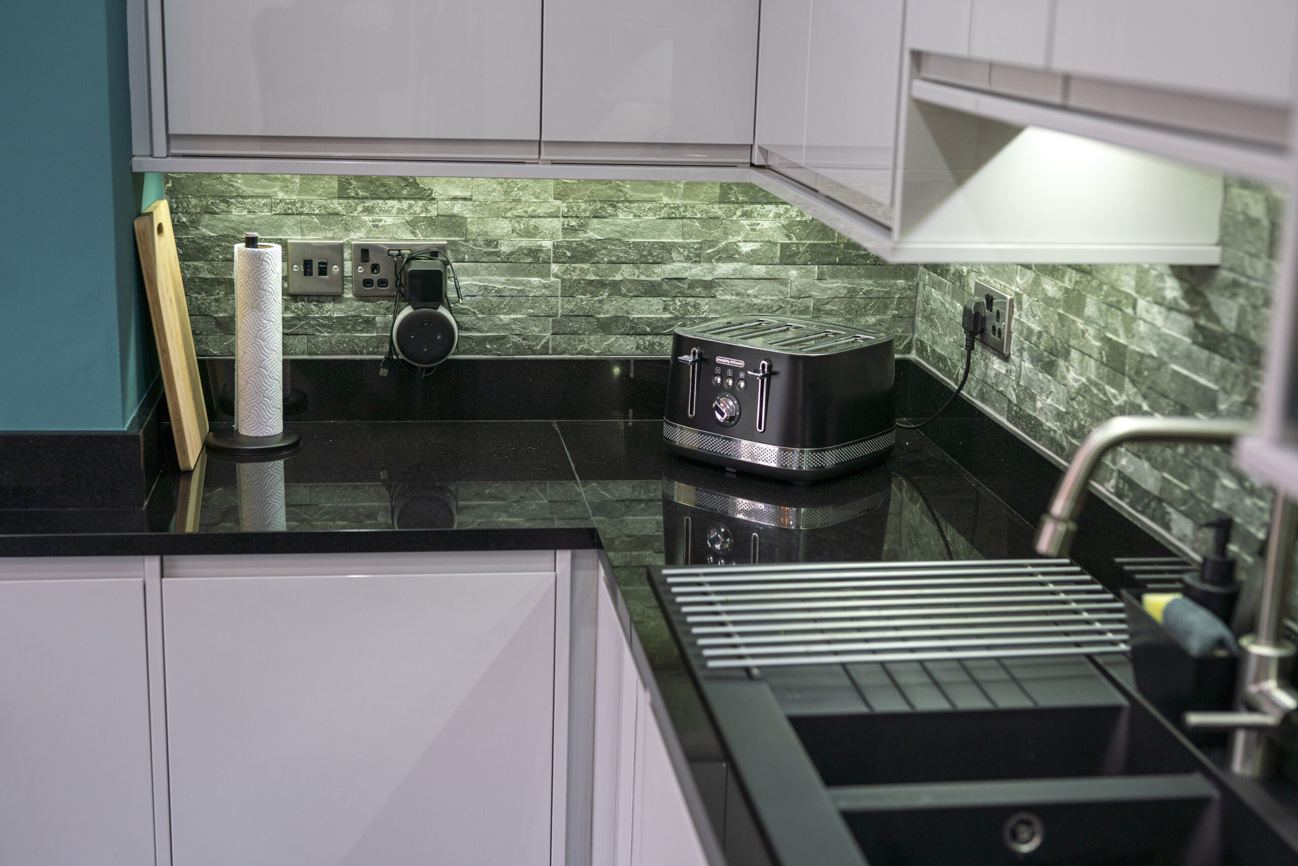 L shaped kitchen corner with Absolute Black Granite worktops and matching Granite upstand, showing the draining board and polished surface beside small appliances.