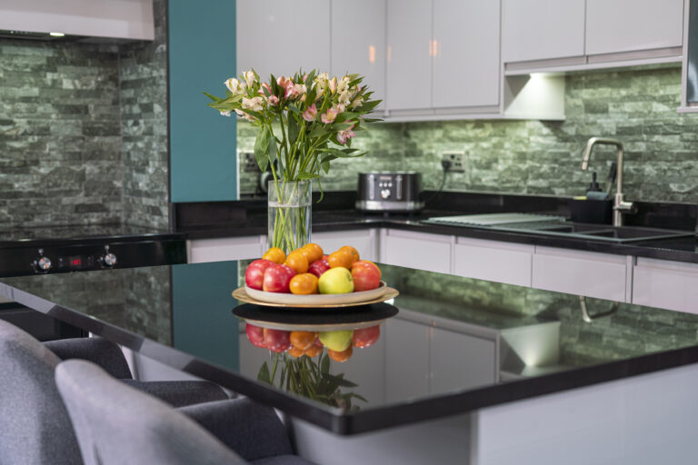 Angled view of an Absolute Black Granite island worktop with a fruit bowl and vase of flowers, showing the polished surface and clean edges.