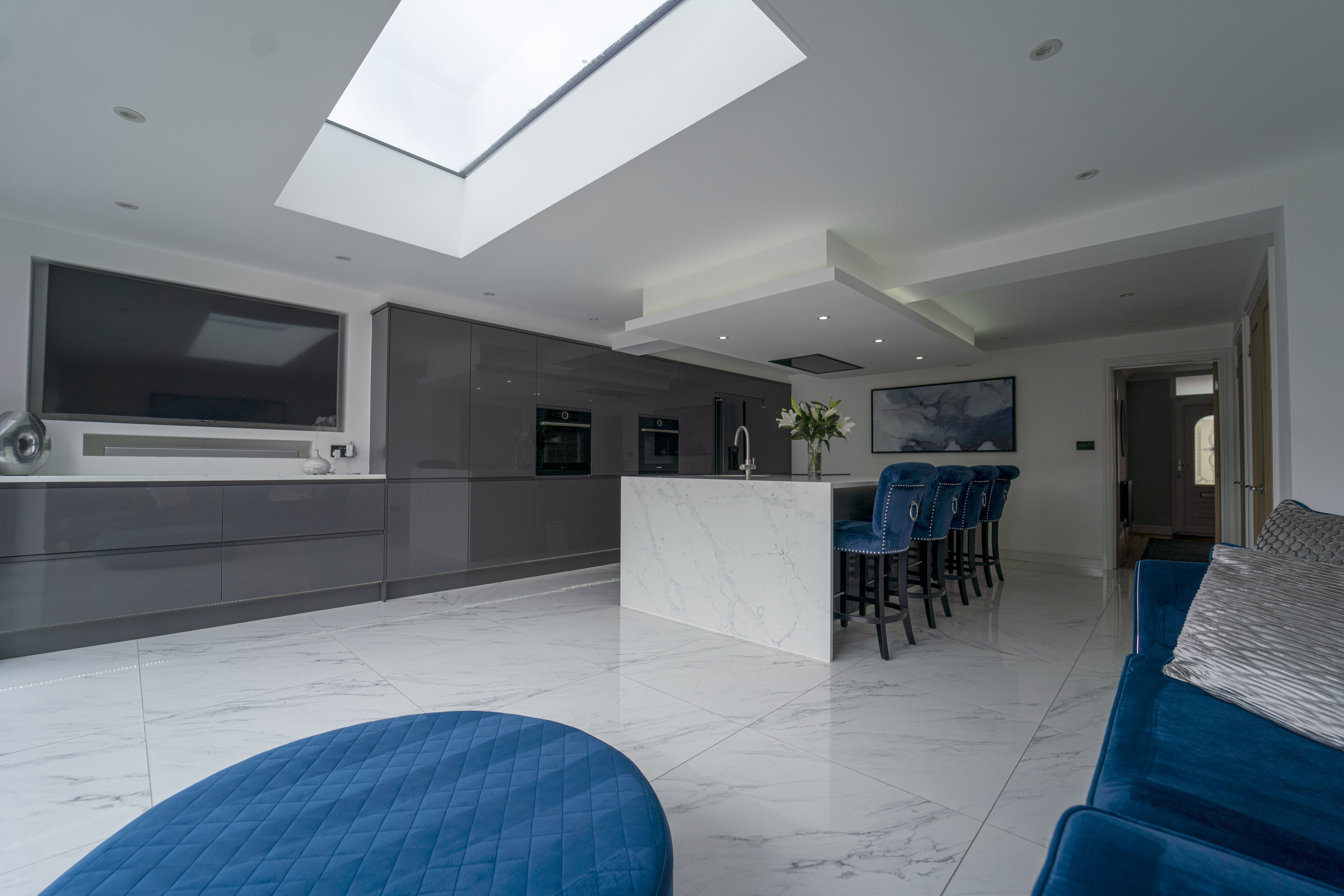 Modern open plan kitchen with White Calacatta Quartz island and blue bar stools under a large skylight
