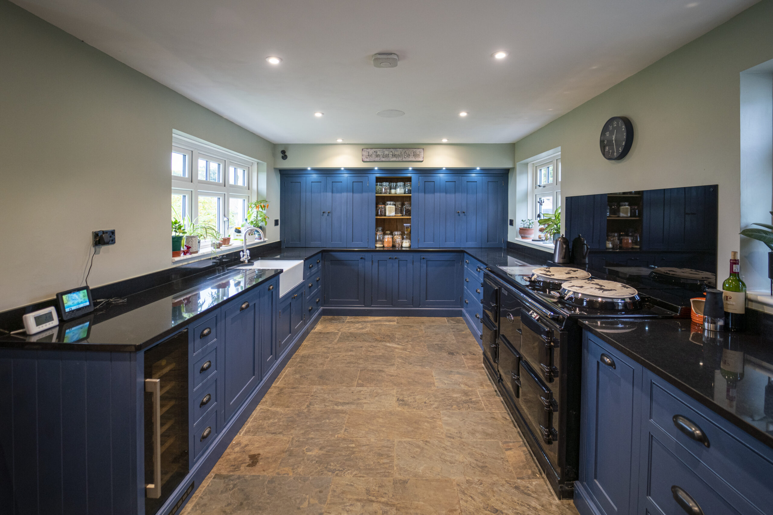 Wide view of a large kitchen with Absolute Black Granite worktops on both sides, blue cabinetry and a central range cooker, showing the full room layout.