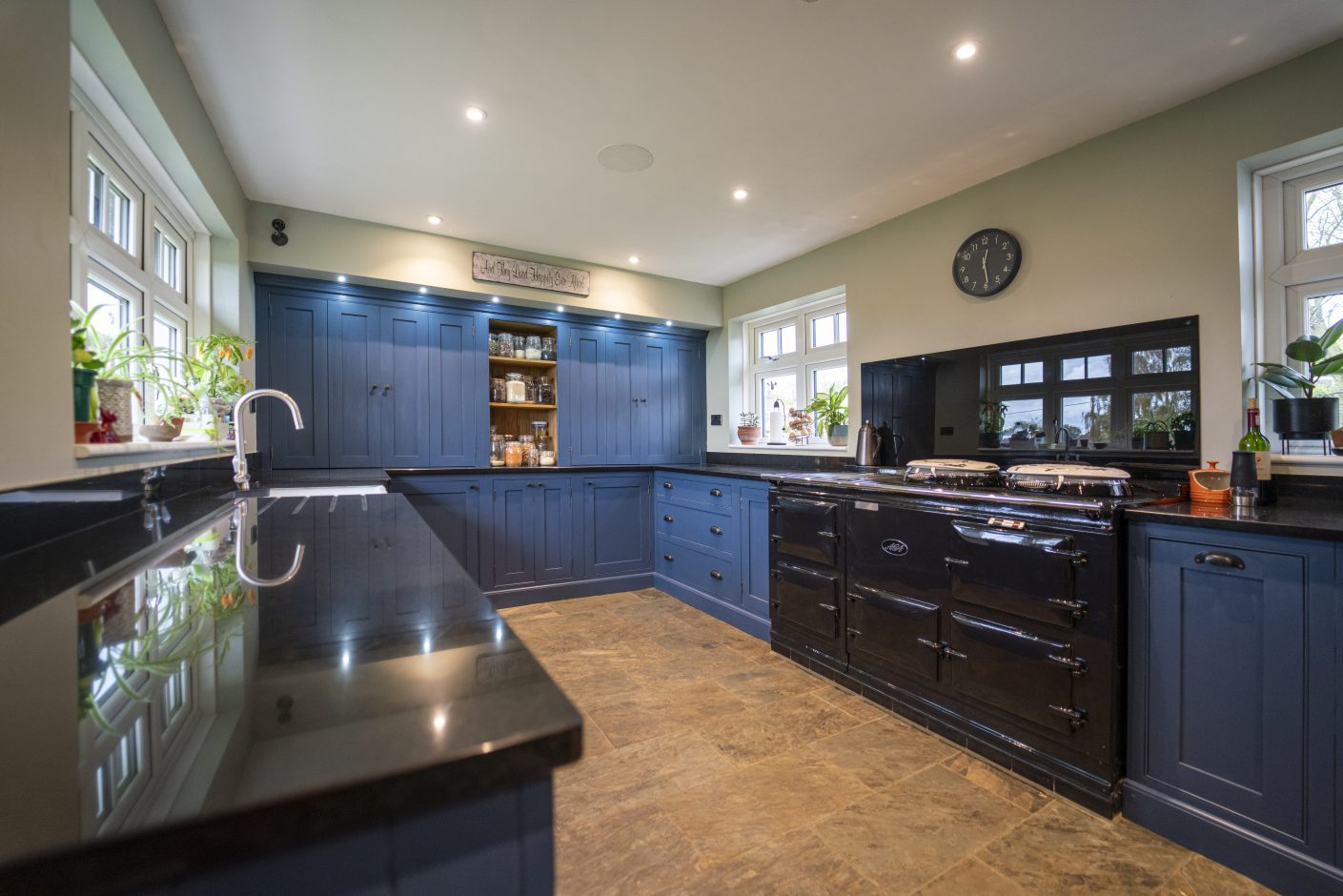 Wide angle view of a blue kitchen with Absolute Black Granite worktops, showing the sink run in the foreground and the main cooking area with a range cooker.
