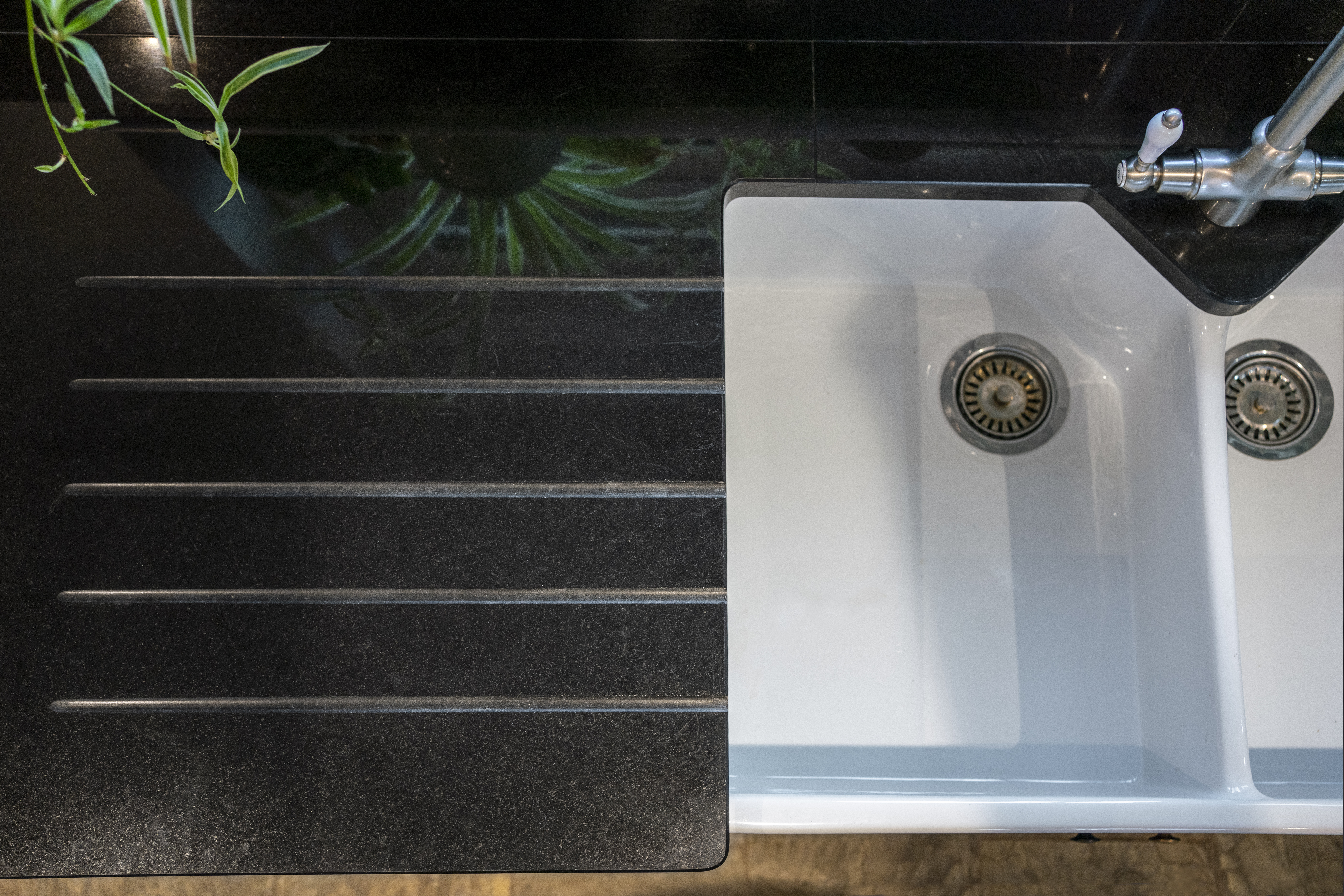 Close up of Absolute Black Granite worktop with precision cut drainer grooves next to a white sink, showing the polished finish and clean lines.